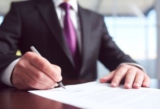 Businessman signing an official document at a desk – NRIWAY company services.